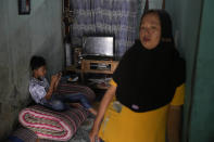 Asiyah stands in the living room of her rented house as her son Muhammad Ibnu Rosihin plays video games on a mobile phone, in Semarang, Central Java, Indonesia, Sunday, Sept. 4, 2022. For years the tide would flood Asiyah's home along the northern coast of Java, Indonesia. Rising seas and stronger tides as an effect of climate change had destroyed her village's crops and washed away dirt paths people walked along. (AP Photo/Dita Alangkara)