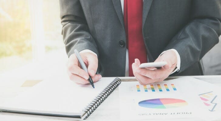 Image shows the hands of a financial professional who is working at a desk. They are making some calculations about investment management fees using a calculator and charts.