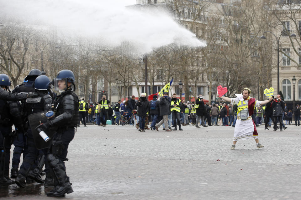 A demonstrator faces police water cannons, Saturday, March 16, 2019 in Paris. French yellow vest protesters clashed Saturday with riot police near the Arc de Triomphe as they kicked off their 18th straight weekend of demonstrations against President Emmanuel Macron. (AP Photo/Christophe Ena)