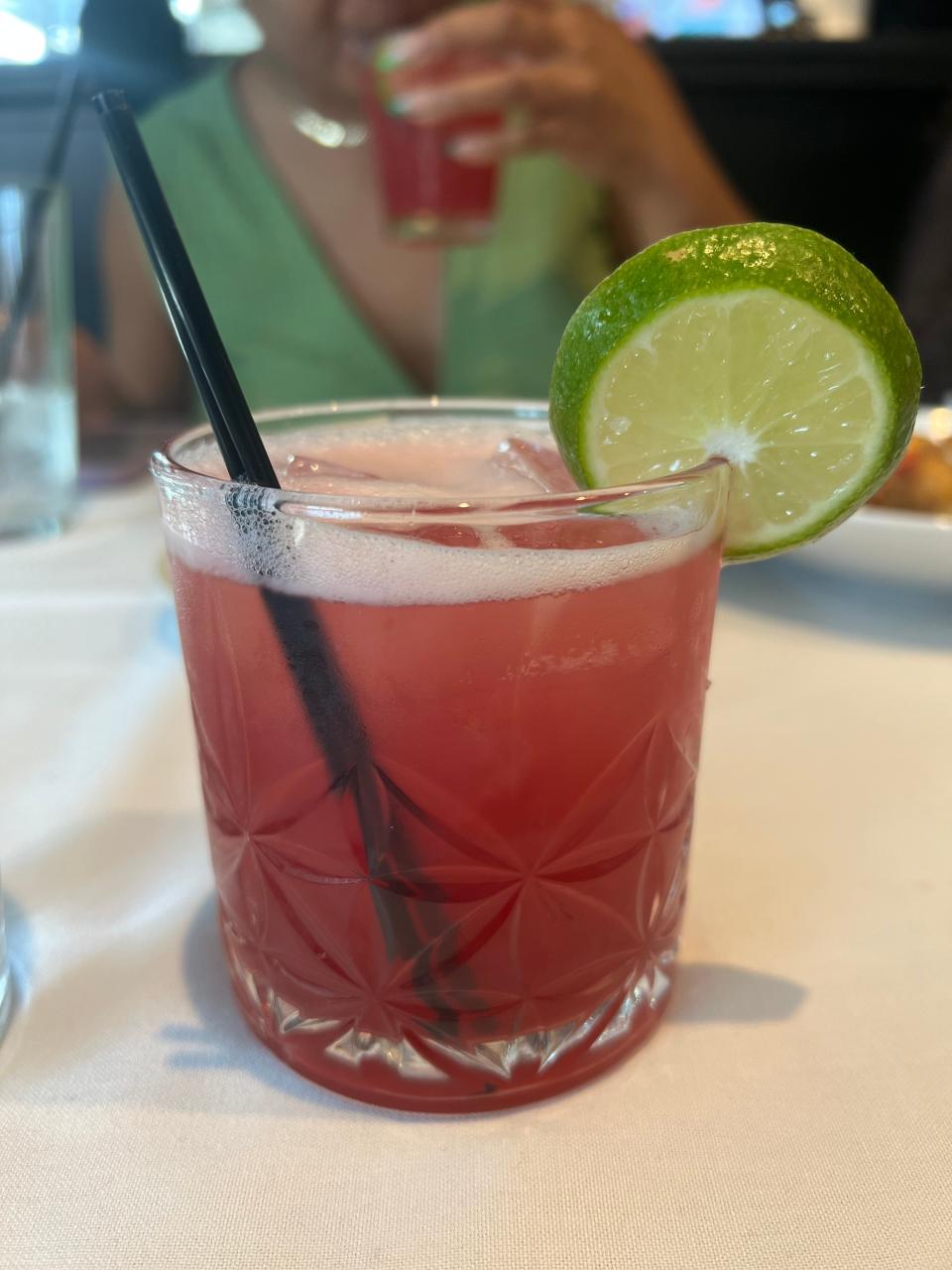 Close-up of a refreshing drink with a lime slice, served on a table with a person in the background