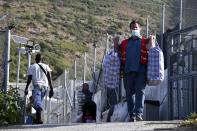 A man carries the belongings of migrants as they leave from an overcrowded refugee camp at the port of Vathy on the eastern Aegean island of Samos, Greece, Monday, Sept. 20, 2021. The transfer of all the migrants to the new €43 million ($50 million) closed monitored facility began Monday and be completed by Wednesday. (AP Photo/Michael Svarnias)