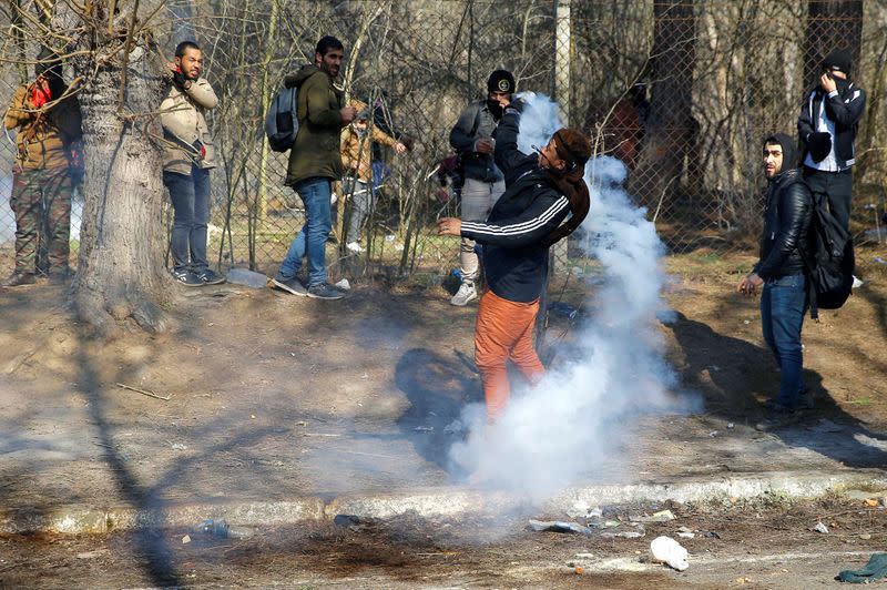 A migrant throws a tear gas canister back during clashes with Greek police, at the Turkey's Pazarkule border crossing with Greece's Kastanies, in Edirne