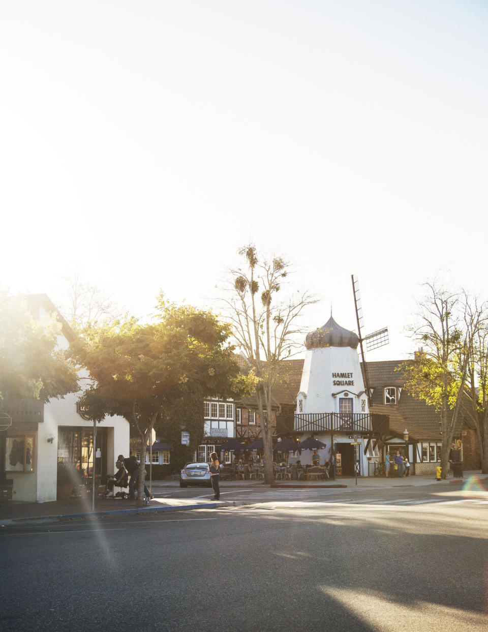 Sunlit street with pedestrians near a building with a windmill structure on its roof