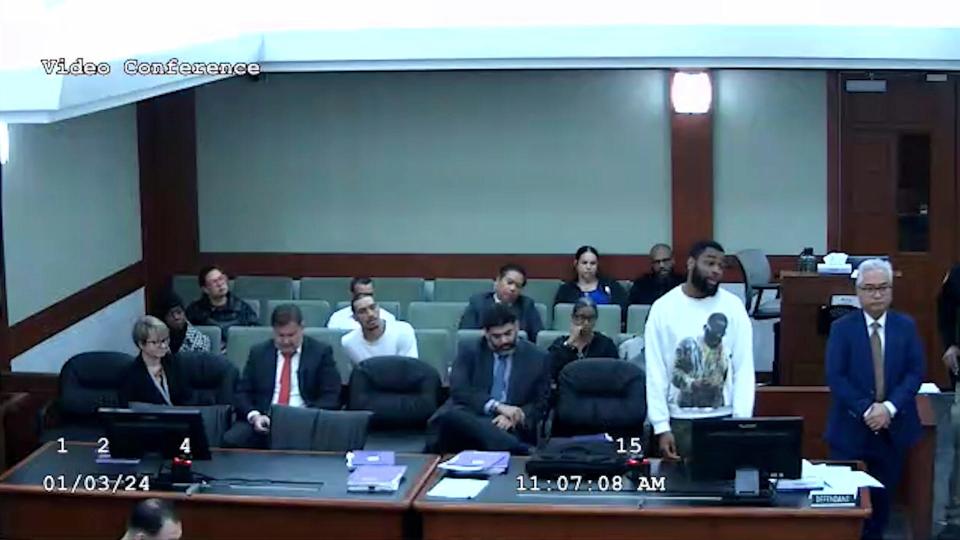 In this image from video provided by the Clark County District Court, defendant Deobra Redden in a white long-sleeved shirt is seen standing next to his defense attorney at his sentencing in a felony battery case, Wednesday, Jan. 3, 2024 in Las Vegas. The image shows the defendant before he launched over Clark County District Court Judge Mary Kay Holthus' desk, starting a fight with courtroom officers and staff, according to the video and court officials.