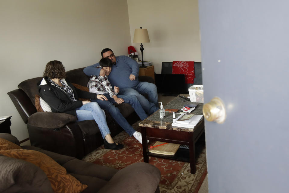 FILE - In this March 24, 2020, file photo, Sonia Bautista, left, watches as husband William Gonzalez, right, hugs their son Ricardo Bautista, while sheltering in their apartment in South San Francisco. On the morning of March 15, as Italy became the epicenter of the global coronavirus pandemic, a half dozen high-ranking California health officials held an emergency conference call to discuss a united effort to contain the spread of the virus in the San Francisco Bay Area. That call and the bold decisions that came in the hours afterward have helped California avoid the kind of devastation from the virus in parts of Europe and New York City. (AP Photo/Jeff Chiu, File)