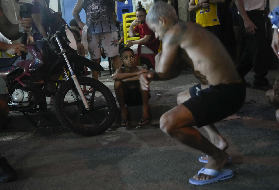 FILE - A boy watches youth perform the street dance style known as passinho in the Rocinha favela of Rio de Janeiro, Brazil, April 11, 2024. Passinho or "little step" began with small groups performing at parties inside Rio's favelas, but has since spread, helping to break the stigma of the communities often known for violence and drug gangs. (AP Photo/Silvia Izquierdo, File)