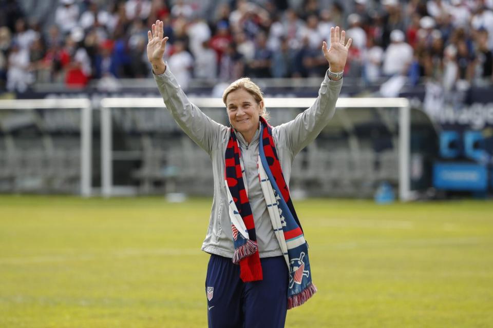 Jill Ellis raises her hands on the pitch.