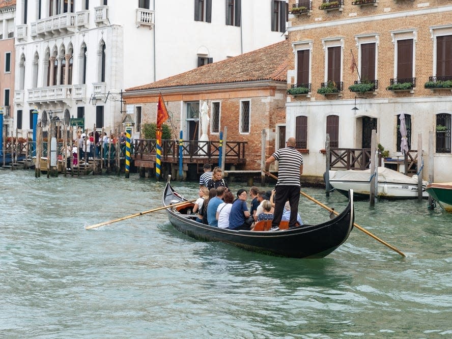 Two gondoliers in striped shirts guide a gondola full of people in Venice.