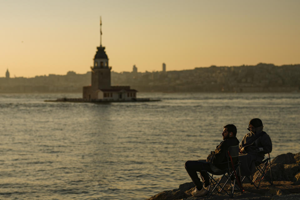 People sit near the Maiden's Tower as the sun sets at the Bosphorus, in Istanbul, Turkey, Saturday, March 23, 2024. (AP Photo/Emrah Gurel)