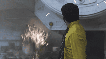 A man in a yellow jacket looks away from an explosion in a futuristic spaceship setting
