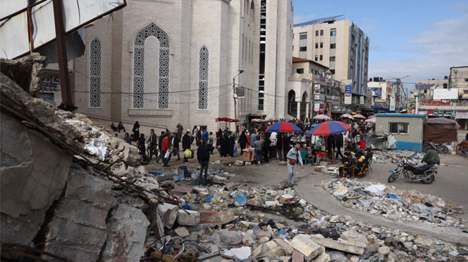 People walk pass market stalls and destroyed buildings in Khan Younis