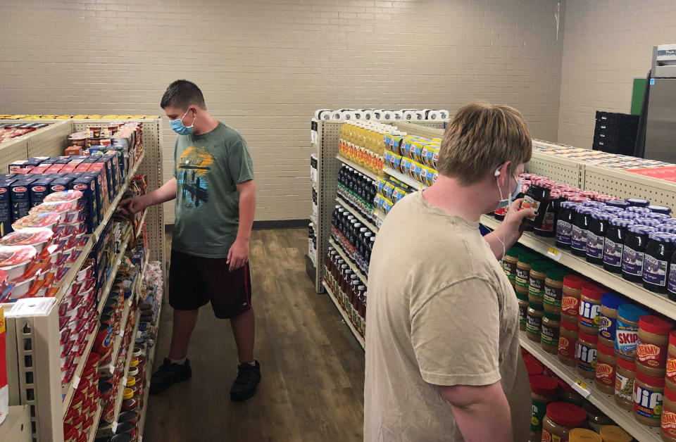 In this photo provided by Anthony Love, student Hunter Weertman, 16, left, stocks shelves and takes inventory while working as a manager of the student-led free grocery store at Linda Tutt High School on Nov. 20, 2020, in Sanger, Texas. The store provides food, toiletries and household items to students, faculty and community members in need. (Anthony Love via AP)
