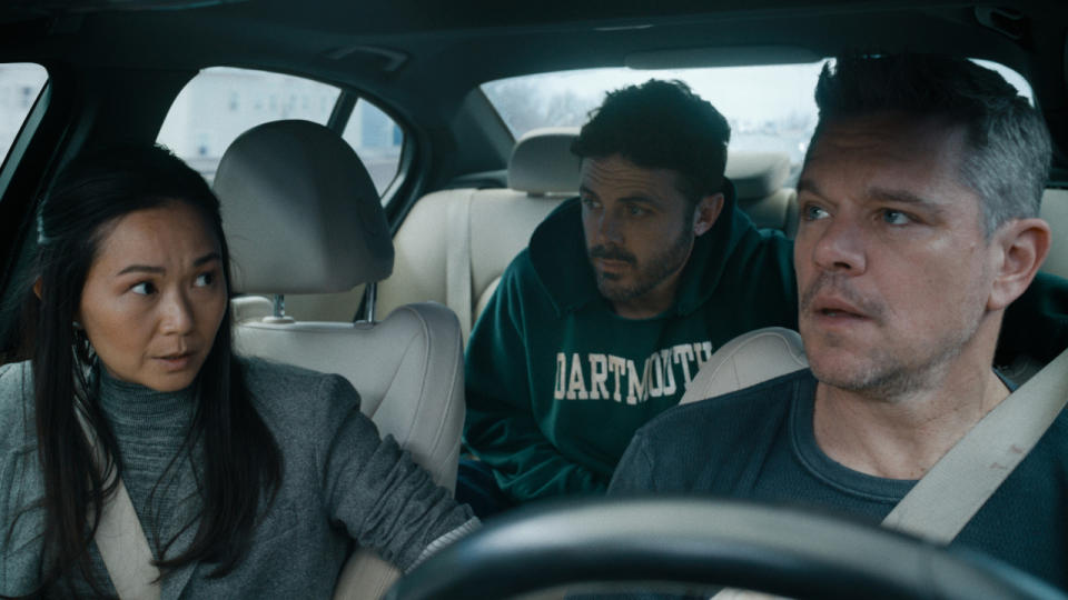 Hong Chau speaks with Matt Damon in the front of a car, while Casey Affleck watches in The Instigators.