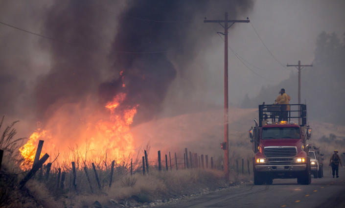 A makeshift fire truck shoots water on a wildfire from the road.