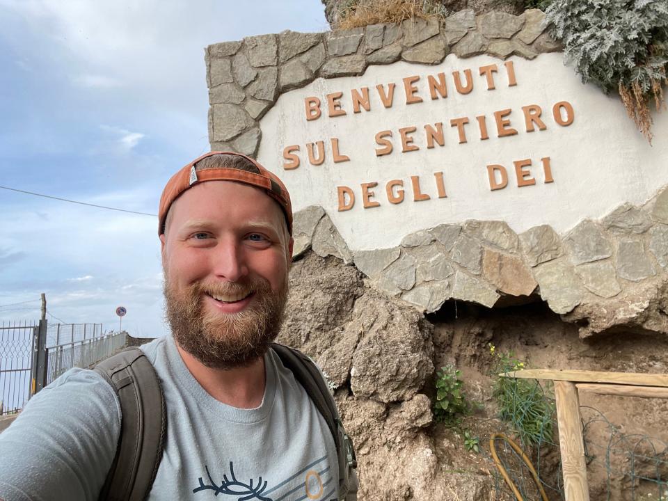 Trent poses for a selfie in front of a sign that reads "Benvenuti Sul Sentiero Degli Dei."