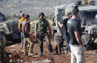 Israeli settlers stand next to military vehicles during a Palestinian protest against the expansion of Jewish settlements near the West Bank town of Salfit, Monday, Nov. 30, 2020. In years to come, Israelis will be able to commute into Jerusalem and Tel Aviv from settlements deep inside the West Bank via highways, tunnels and overpasses that cut a wide berth around Palestinian towns. Rights groups say the new roads that are being built will set the stage for explosive settlement growth, even if President-elect Joe Biden's administration somehow convinces Israel to curb its housing construction. (AP Photo/Majdi Mohammed)