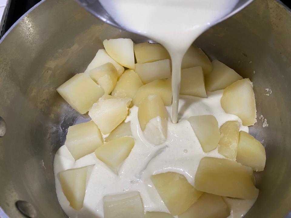 pouring creamy liquid over a pot of cooked potato chunks