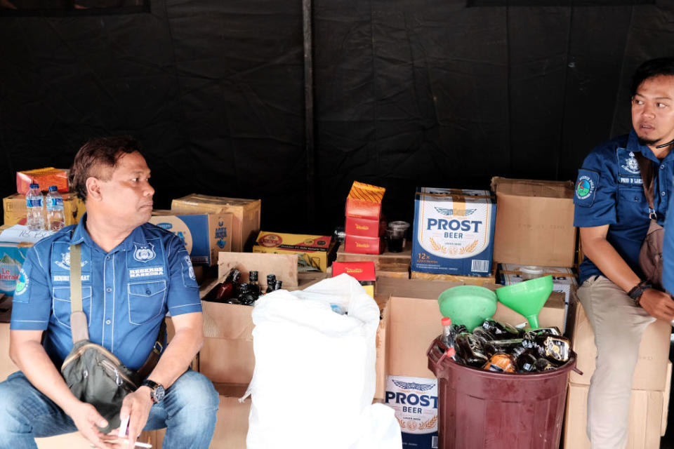 Photos show Indonesian police guards sitting with a stock of recently seized bootleg liquor in 2018.