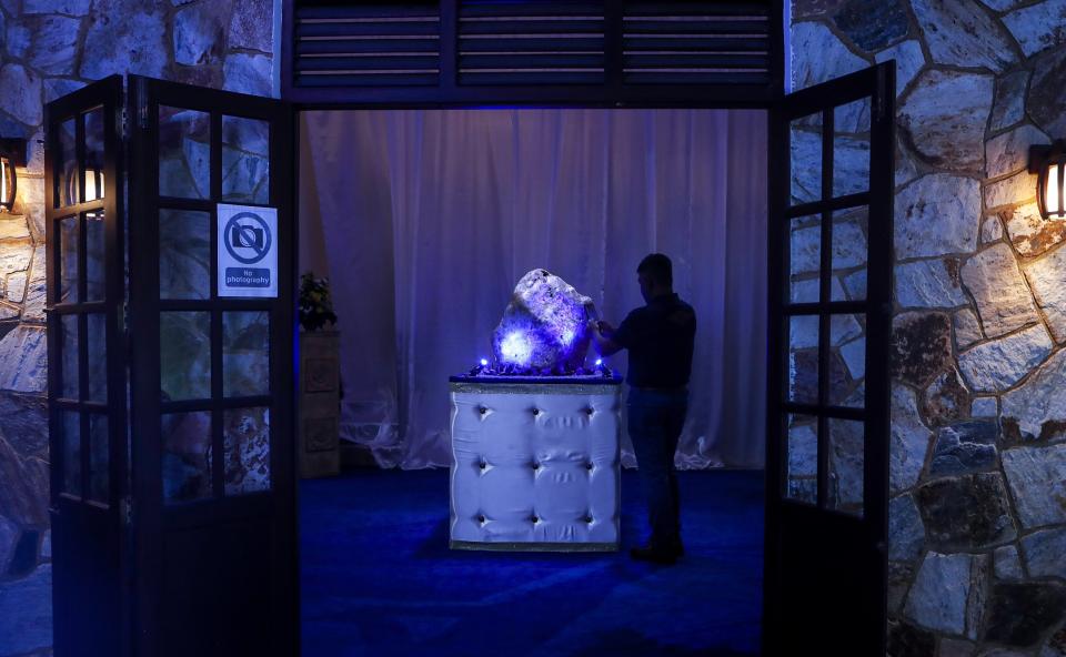 A Sri Lankan man takes a photo of a 310 kilograms (683 pounds) heavy natural corundum blue sapphire at a residence where it is kept in Horana, about 41 kilometers (25 miles) south of Colombo, Sri Lanka, Sunday, Dec. 12, 2021. A gem company in Sri Lanka has unveiled the massive gemstone that is certified as a rare and one of the biggest corundums found in the country and plans to offer it to museums and gem collectors. (AP Photo/Eranga Jayawardena)