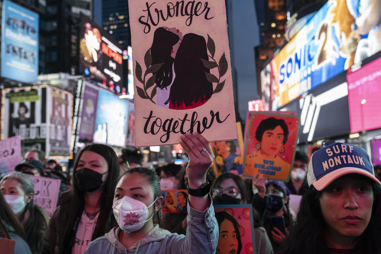 Asian American women at a rally hold up signs reading: Stronger together.