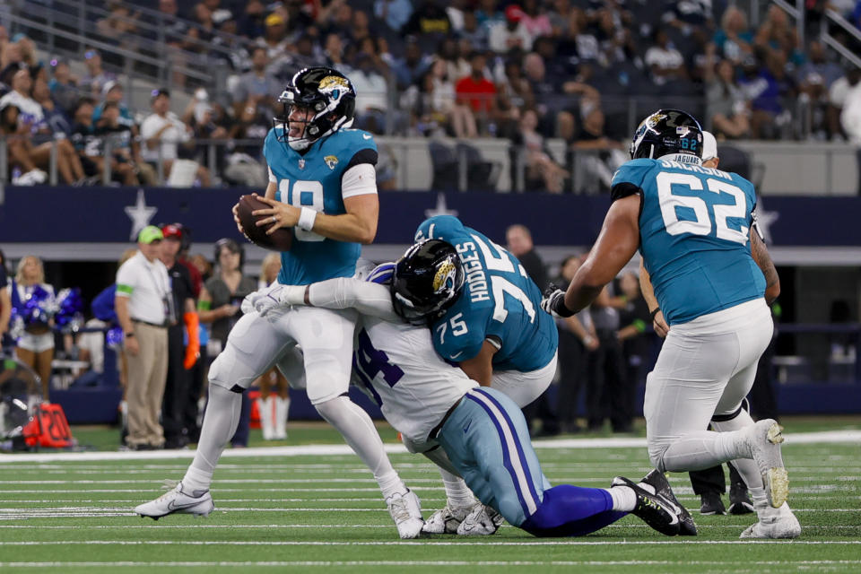 ARLINGTON, TX - AUGUST 12: Jacksonville Jaguars quarterback Nathan Rourke (18) has Dallas Cowboys defensive end Ben Banogu (94) wrapped around his legs during the preseason game between the Dallas Cowboys and the Jacksonville Jaguars on August 12, 2023 at AT&T Stadium in Arlington, Texas. (Photo by Matthew Pearce/Icon Sportswire via Getty Images)