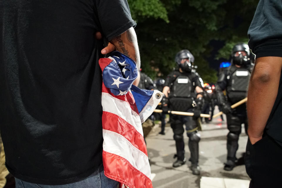 A protester holds a tattered American flag as police stand guard over the old state capitol in in Raleigh, N.C., on Sunday, May 31, 2020. It was the second day of protests in the North Carolina capital following the death of Minnesotan George Floyd while in police custody. (AP Photo/Allen G. Breed)