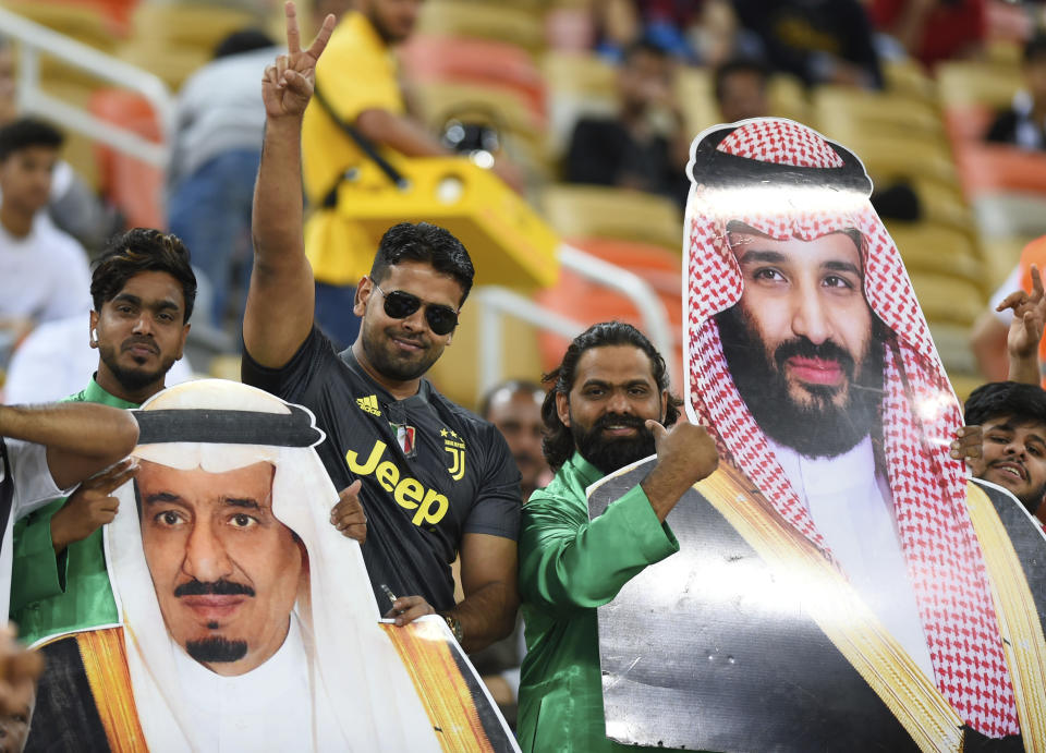 Saudi fans holds pictures of Saudi Arabia's King Salman, left, and Saudi Crown Prince Mohammed bin Salman ahead of the Italian Super Cup final soccer match between AC Milan and Juventus at King Abdullah stadium in Jiddah, Saudi Arabia, Wednesday, Jan. 16, 2019. (AP Photo)