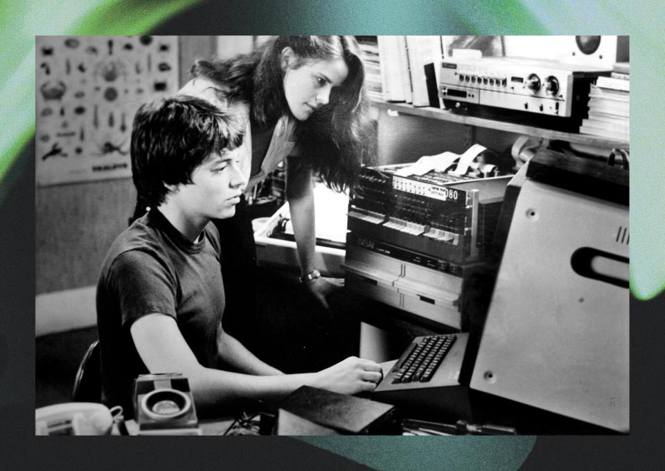 A teen boy sits at a computer with a teen girl leaning over him to look at the screen in a scene from "War Games."