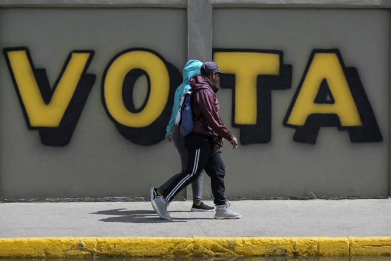 Una pareja camina frente a un gratifi que dice "vota" como parte de las elecciones presidenciales en Venezuela, tomada en Caracas el 27 de julio de 2024 (Yuri CORTEZ)