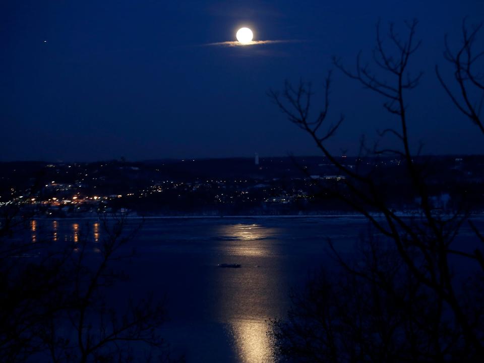 A full moon rises above the Hudson River in a darkened sky