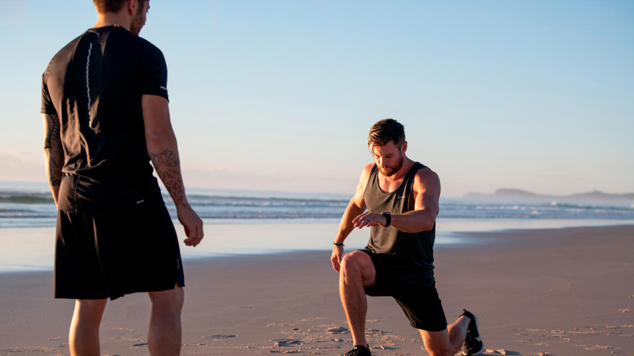  Chris Hemsworth performing lunge exercises on the beach, his trainer Luke Zocchi looks on 