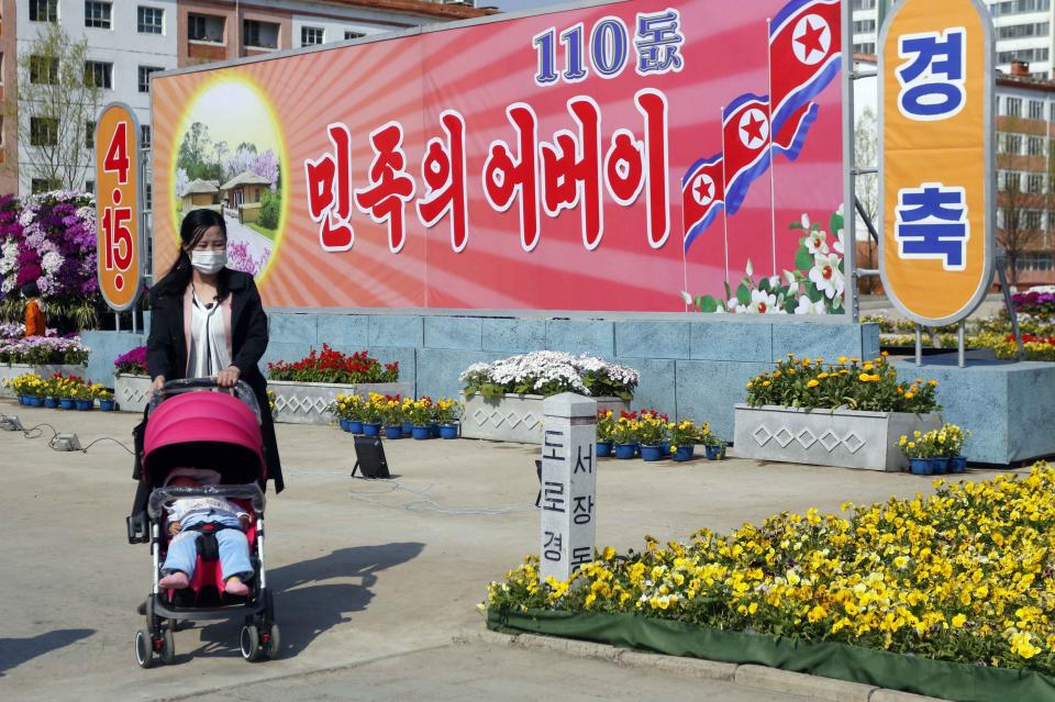 A woman pushes a baby on a stroller in front of the posters marking the 110th birth anniversary of late North Korean leader Kim Il Sung, in Pyongyang, DPRK, on Friday, April 15, 2022. The poster says "Father of Nation". (AP Photo/Jon Chol Jin)