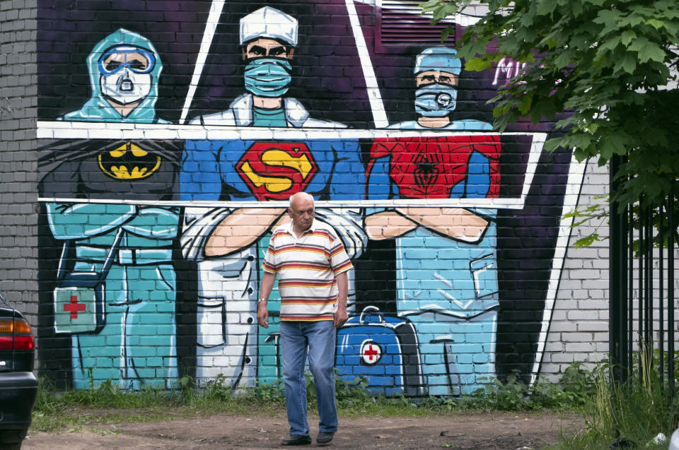 A man walks past a graffiti depicting medical workers struggling with coronavirus as superheroes in Vsevolozhsk, outside St.Petersburg, Russia, Monday, June 15, 2020. (AP Photo/Dmitri Lovetsky)