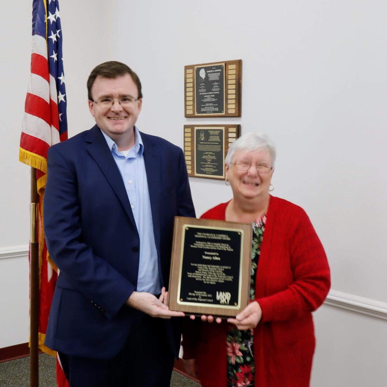 Marshall Town Administrator Forrest Gilliam and current Mayor Nancy Allen stand with a plaque recognizing Allen as the 2023 recipient of Land of Sky's Charles H. Campbell Award for regional leadership.