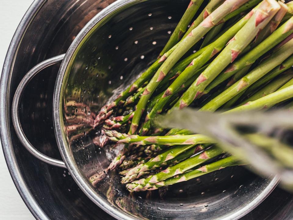 water pouring over asparagus in a stainless steel colander