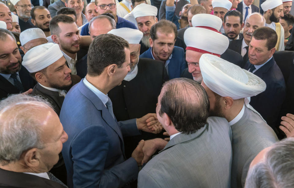 In this photo released by the Syrian official news agency SANA, Syrian President Bashar Assad, center, greets clerics following the prayers of the first day of the the Eid al-Adha, at Afram Mosque in Damascus, Syria, Sunday, Aug. 11, 2019. State news agency SANA showed Assad attending the payers early Sunday at Afram Mosque along with top officials including the prime minister and the country's grand mufti. (SANA via AP)