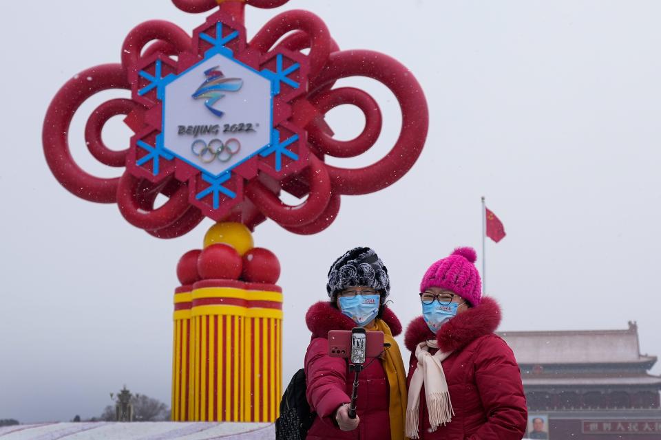 Women wearing face masks printed with a slogan for Beijing Winter Olympics Games take a selfie at Tiananmen Square in Beijing, Jan. 20.