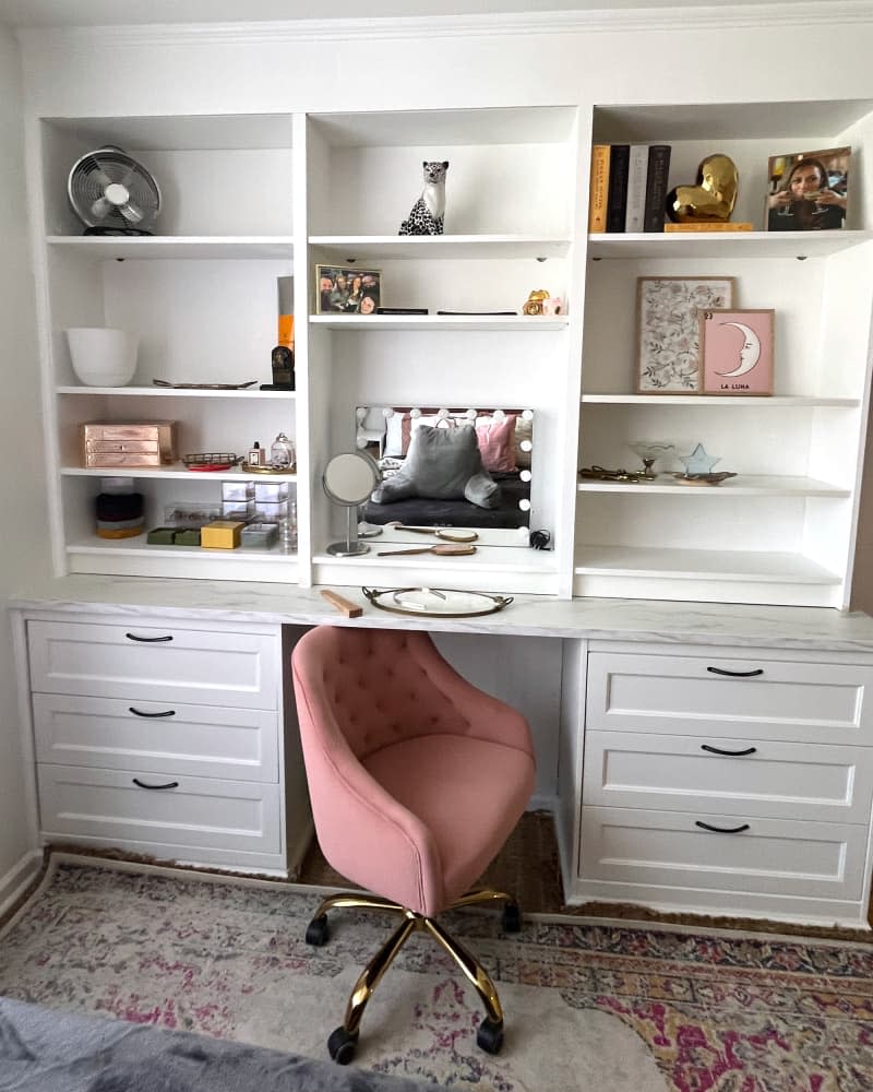 Pink chair at marble top of white wooden shelving and drawers.