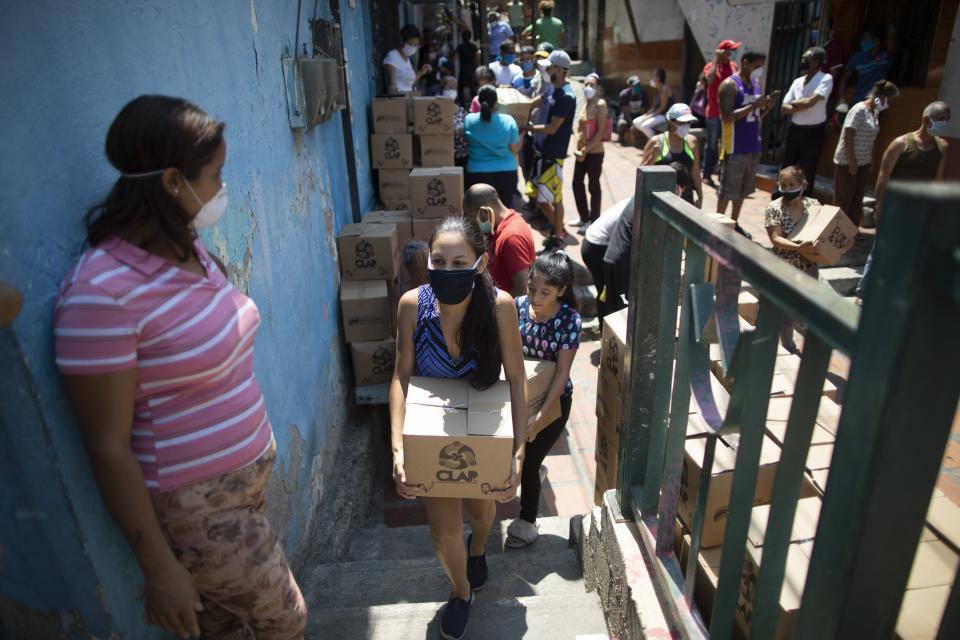 A woman wearing face mask against the spread of the new coronavirus, carries a box of basic food staples such as pasta, sugar and flour, provided by a government food assistance program, in Caracas’ slum of Petare, Venezuela, Thursday, April 30, 2020. The program known as Local Committees of Supply and Production, CLAP, provides highly subsidized food for which recipients pay less than the equivalent of $0.50 per box. (AP Photo/Ariana Cubillos)