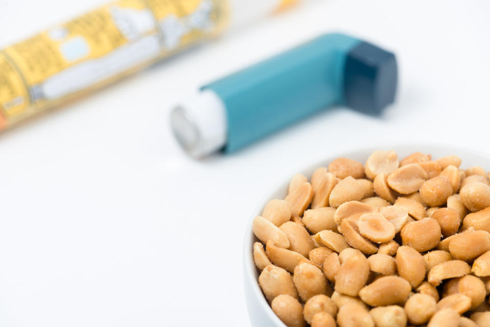 A bowl of peanuts next to an inhaler and an EpiPen on a table