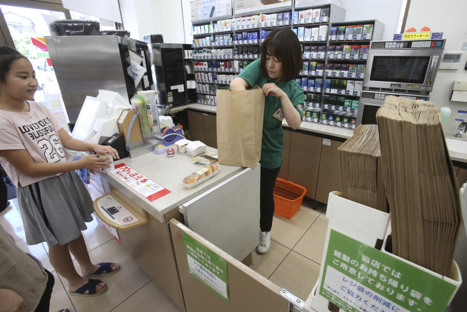 In this June 17, 2019, photo, a salesclerk puts goods into a paper bag after a customer purchased them, at a Seven-Eleven store in Yokohama, near Tokyo. Seven & i Holdings Co., a major Japanese convenience store operator, announced on May, 2019, a plan to replace all plastic shopping bags with paper by 2030 and all plastic packaging with paper, biodegradable or other reusable materials at its nearly 21,000 stores nationwide. Japan, as host of the Group of 20 Summit this weekend, hopes to lead the world in reducing plastic waste. (AP Photo/Koji Sasahara)