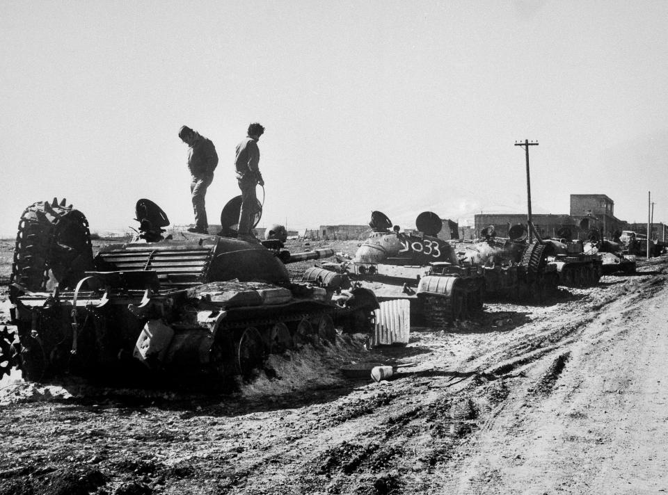 FILE - In this October 1973, file photo, Israeli soldiers look at a long row of burned-out Syrian T-62 tanks hit at the entrance of a village, background, during the Mideast War in the Golan Heights. The Golan front has been mostly quiet since 1974, a year after Syria and Israel fought a war during which Damascus tried unsuccessfully tried to retake the plateau. (AP Photo/File)