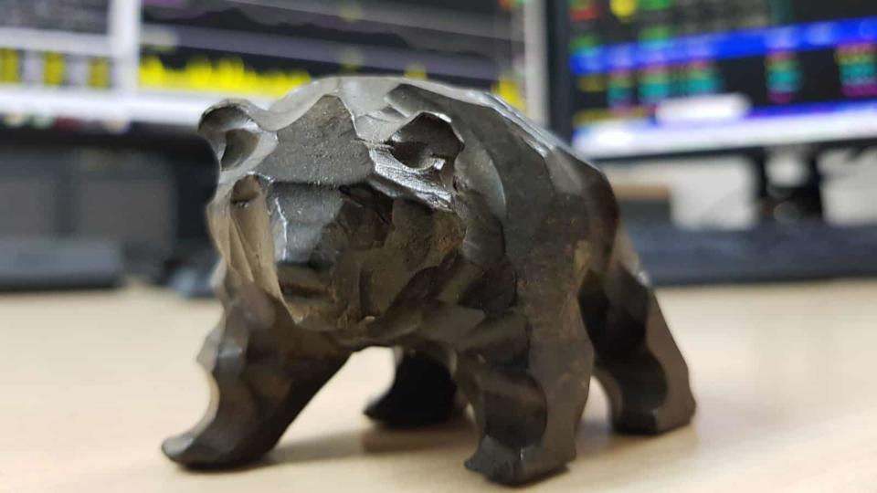 Table model of a bear on the desk in front of monitors displaying stock prices