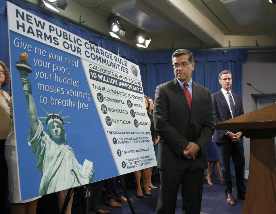 California Attorney General Xavier Becerra, left, glances at a display outlining the supposed effects on immigrants in the state under the Trump administration's new rules blocking green cards for many of those who receive government assistance, during a news conference in Sacramento, Calif., Friday, Aug. 16, 2019. Becerra and Gov. Gavin Newsom, right, announced that California has joined three other states and the District of Columbia in a lawsuit filed Friday against some of the administration's most aggressive moves to restrict legal immigration that are supposed to take effect in October. (AP Photo/Rich Pedroncelli)