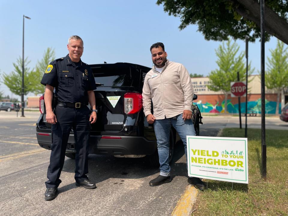 Green Bay Police Chief Chris Davis and Wello's Rogelio Contreras display a Yield to Your Neighbor magnet on a police vehicle and a Yield to Your Neighbor yard sign outside of the department.