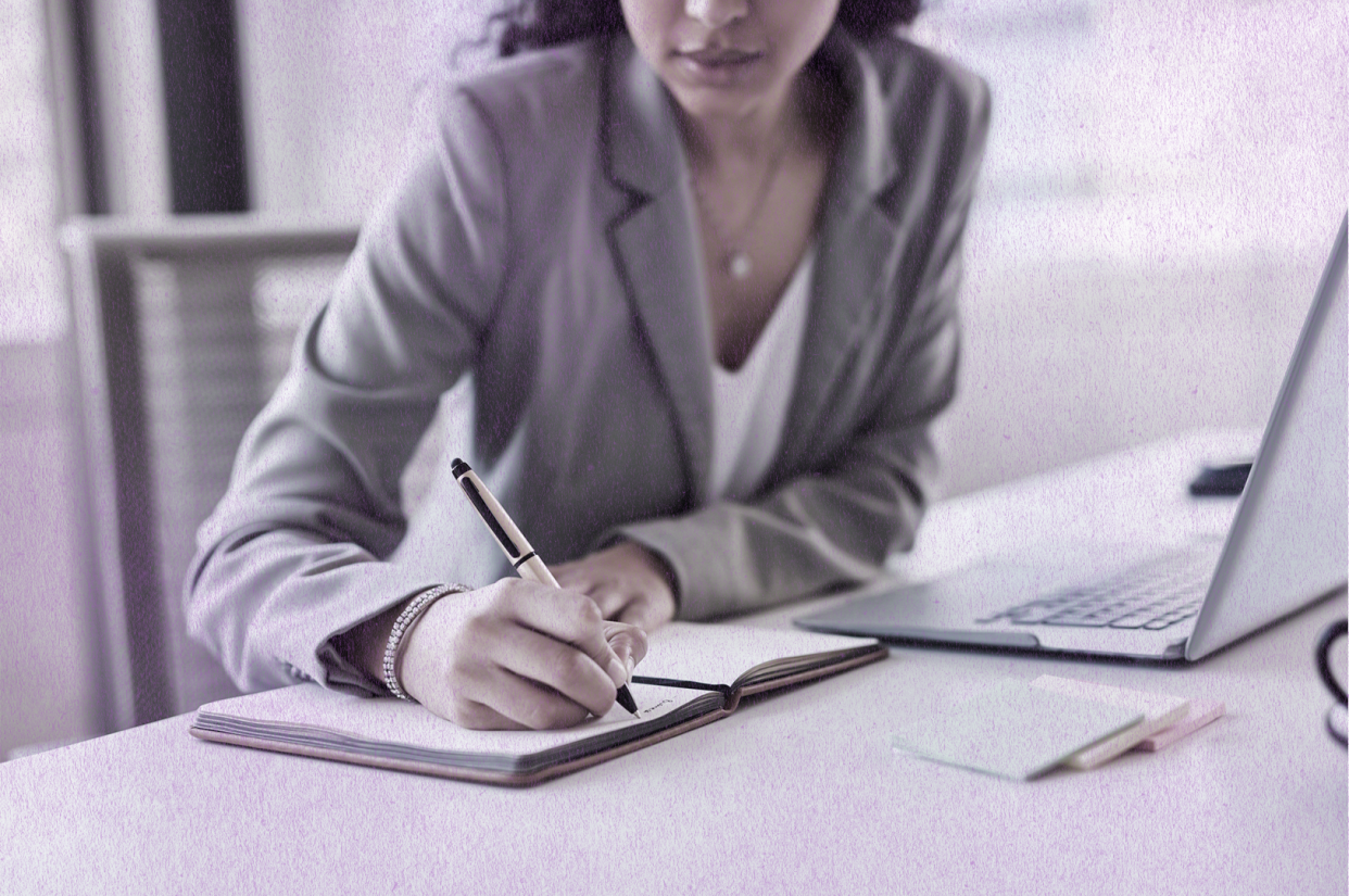 Woman in an office sitting at a desk writing notes in a notebook