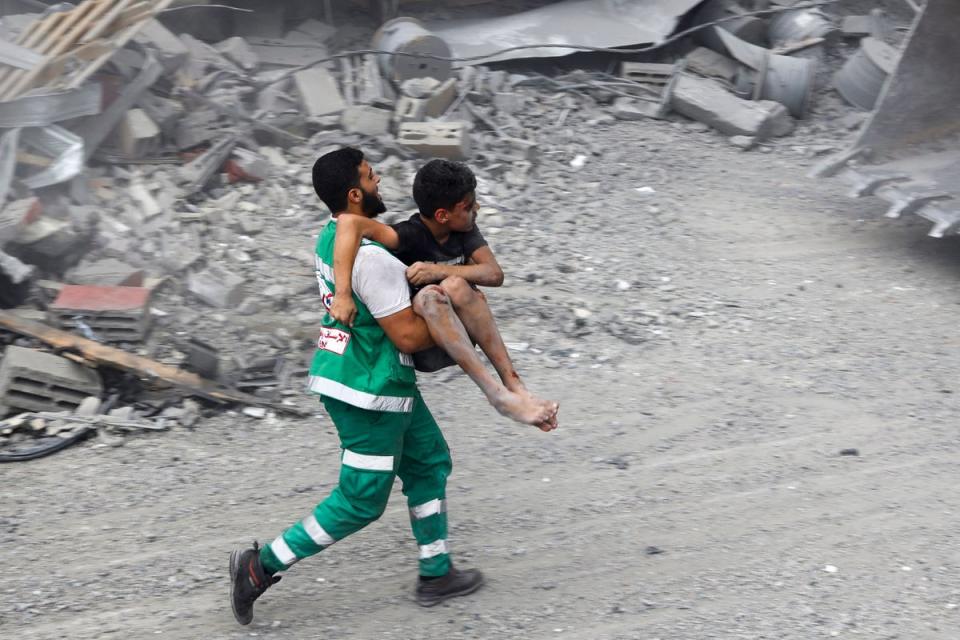 A member of the Palestinian civil defence carries a wounded boy rescued from rubble (AFP via Getty Images)
