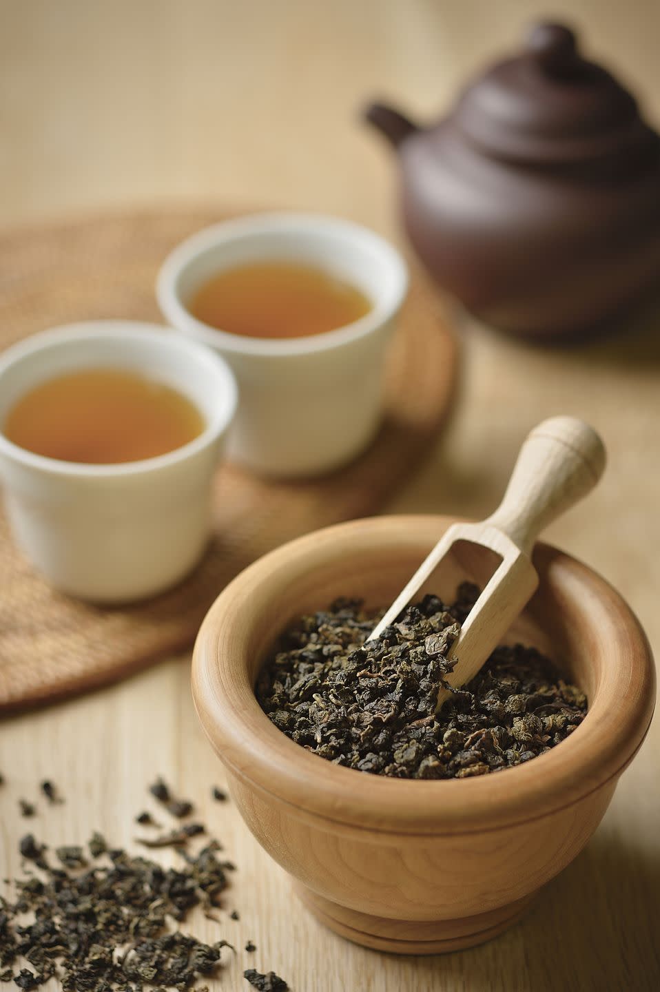 oolong tea leaves spilling out from a wooden bowl near two cups of the brewed tea