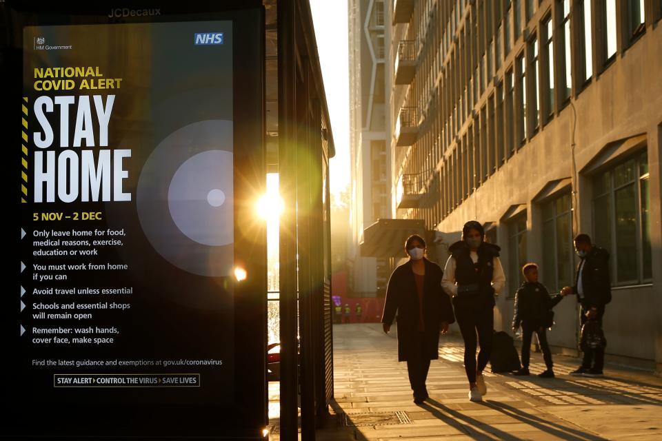 Pedestrians wearing face masks pass a digital display showing the new measures required as England enters a second coronavirus lockdown in central London on November 5, 2020. (Photo by Hollie Adams / AFP) (Photo by HOLLIE ADAMS/AFP via Getty Images)