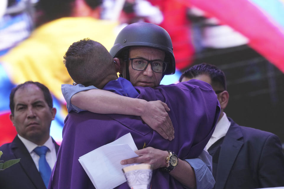 Wearing a bulletproof vest and ballistic helmet, presidential hopeful Christian Zurita, for "Movimiento Construye," who was named to replace the recently slain Fernando Villavicencio, is embraced by a Catholic priest during a Mass prior to his closing campaign rally in Quito, Ecuador, Thursday, Aug. 17, 2023. The upcoming snap election set for Aug. 20 was called after President Guillermo Lasso dissolved the National Assembly by decree in May, to avoid being impeached. (AP Photo/Dolores Ochoa)